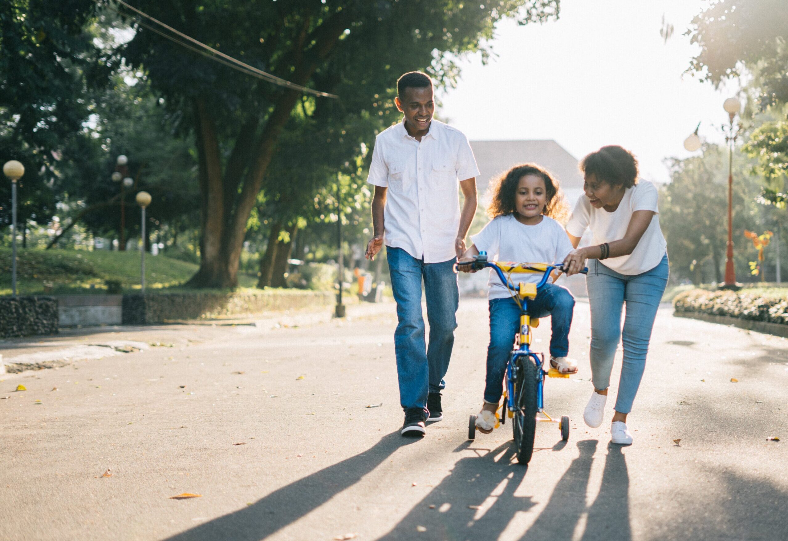 Two black parents teaching their child how to ride a bike, showing the positive effects of family counselling in North York Ontario.